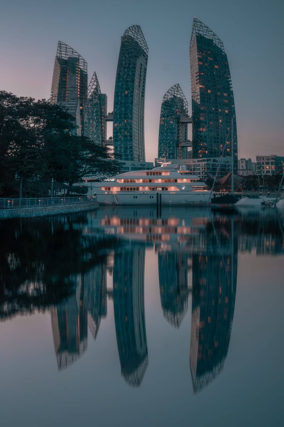 Luxury yacht docked in a marina at dusk with city skyline.